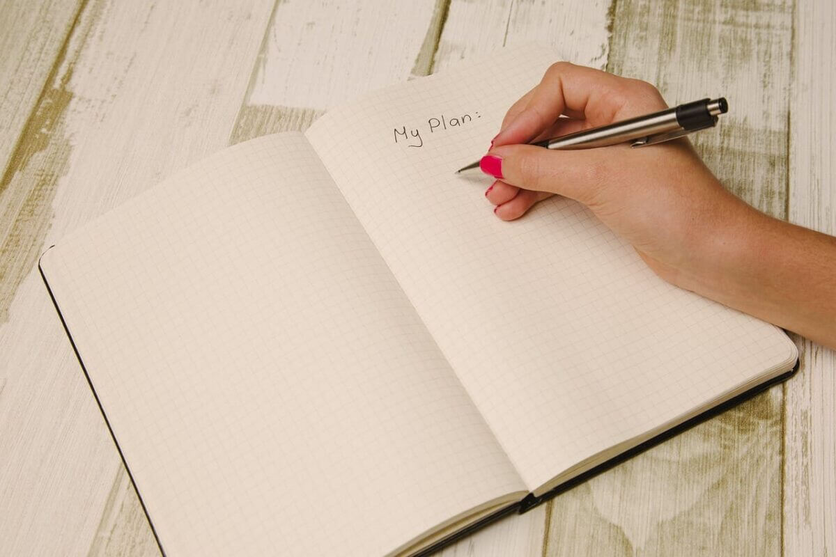 Stock photograph of a person holding a pen, starting a plan in a note pad.